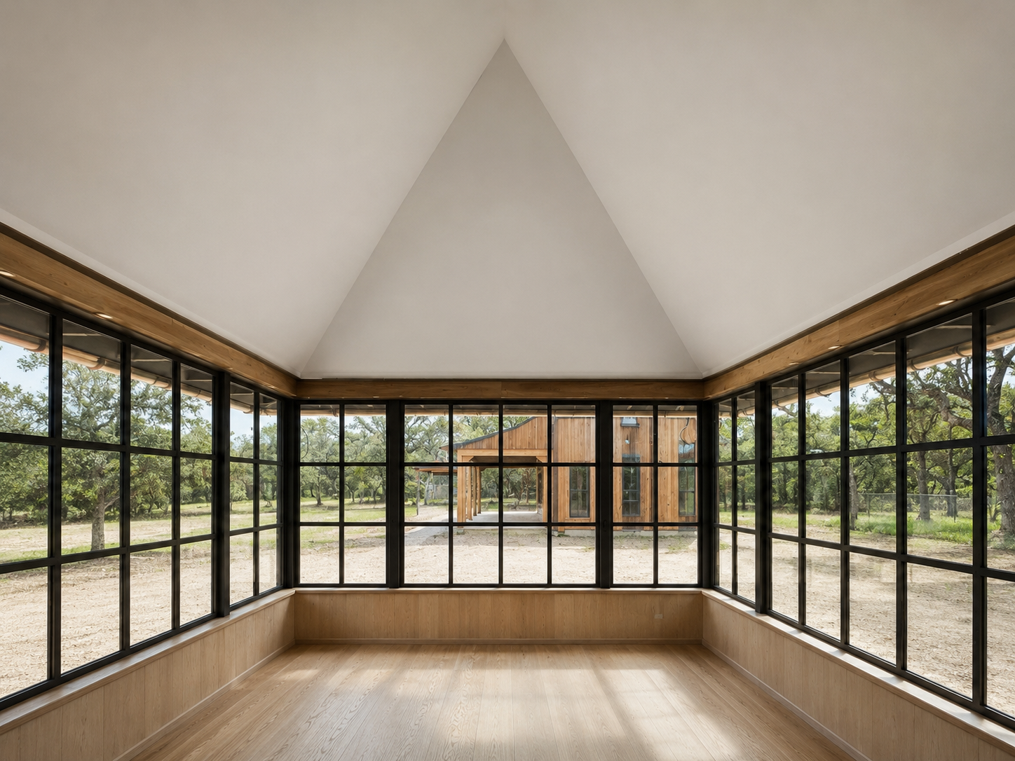 Glass pavilion interior with steel windows, white oak base paneling, and vaulted plaster ceiling